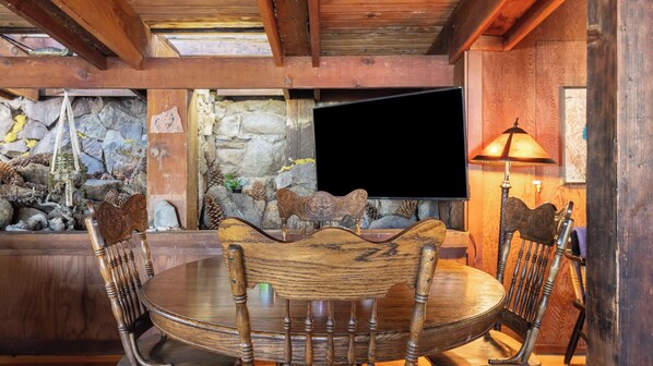 Un comedor rústico con pared de piedra, muebles de madera y televisor.
