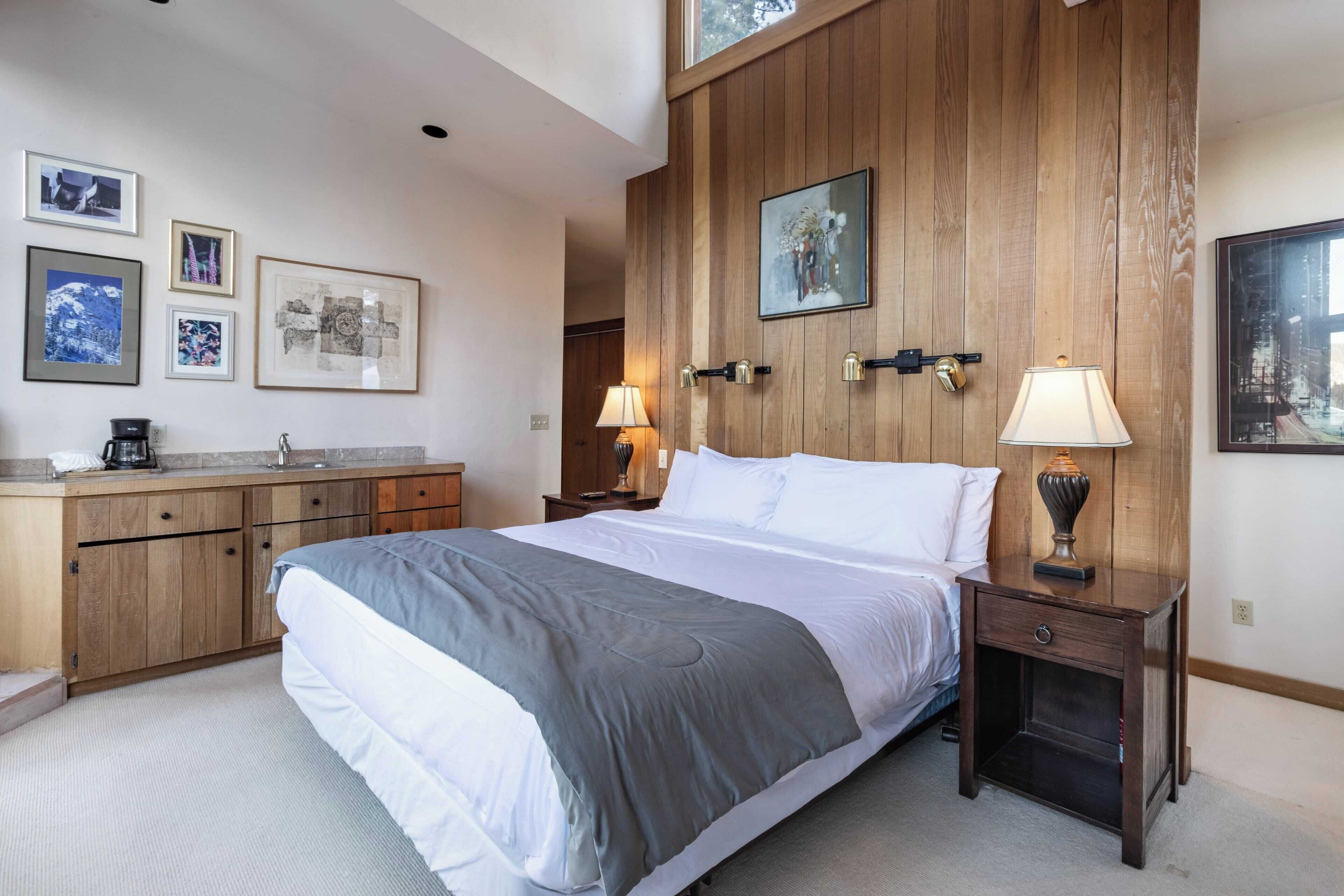 A bedroom with a bed, wooden paneling, a dresser, a nightstand, and framed pictures on the wall.