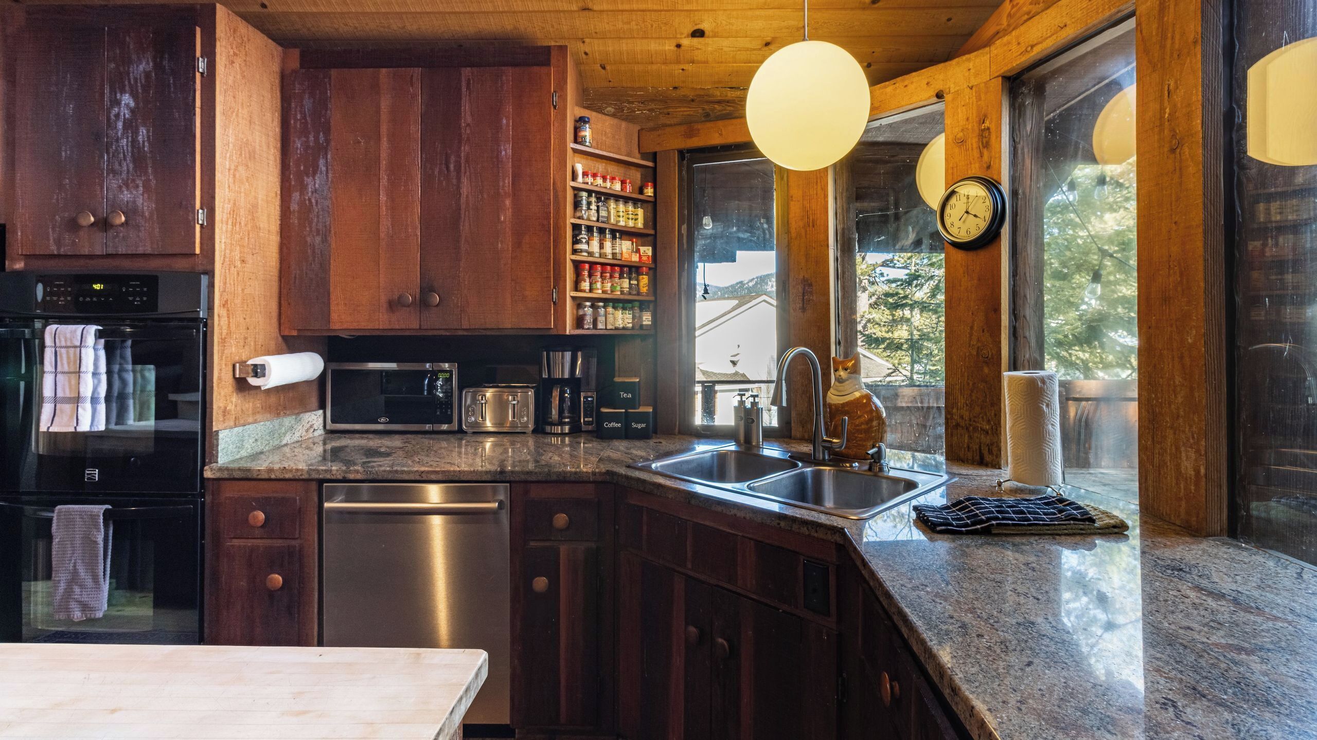 A kitchen with wooden cabinets, stainless steel appliances, a granite countertop, and a window with a view.