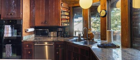 A kitchen with wooden cabinets, stainless steel appliances, a granite countertop, and a window with a view.
