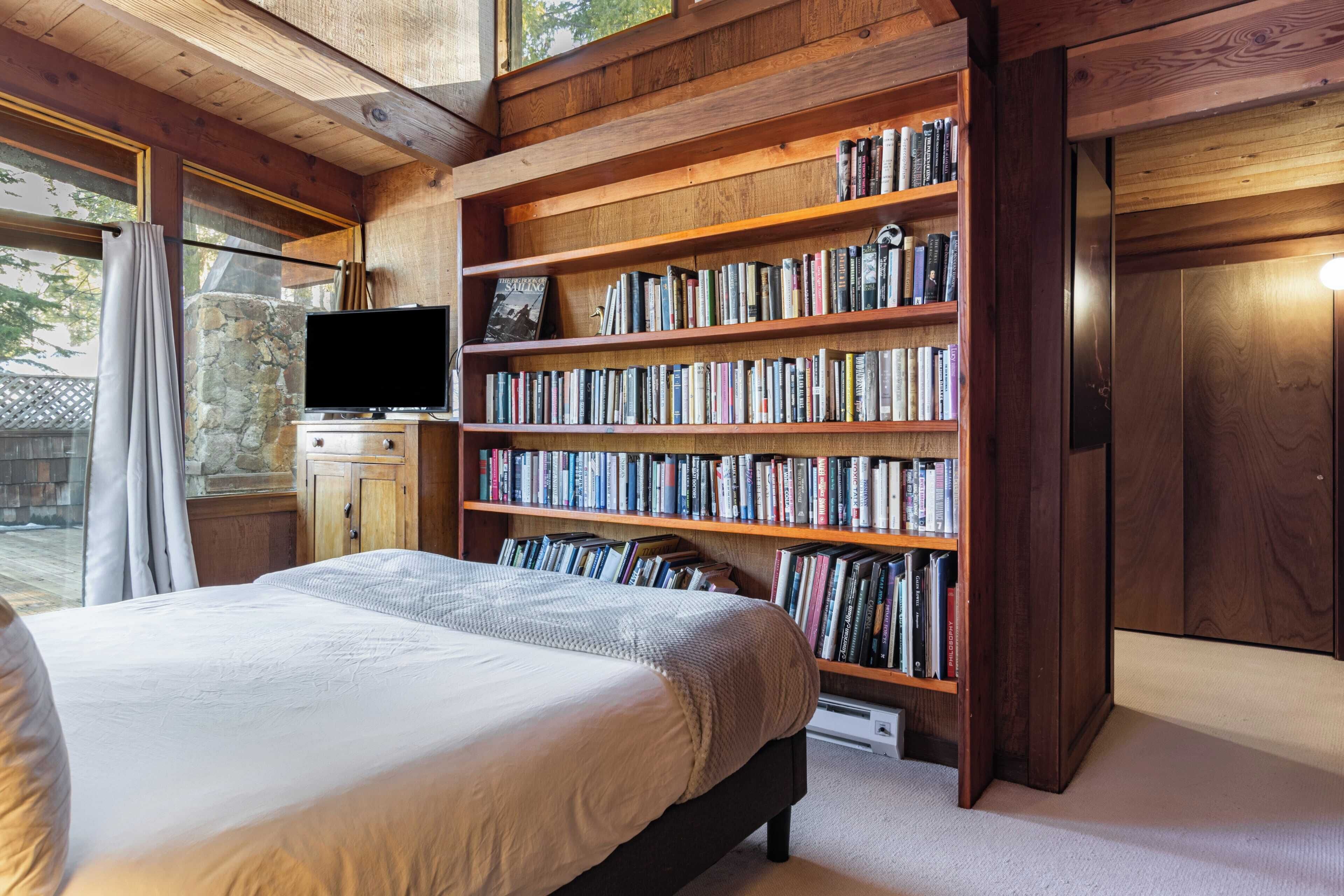 A bedroom with a large bed, a bookshelf filled with books, a television, and a stone wall.