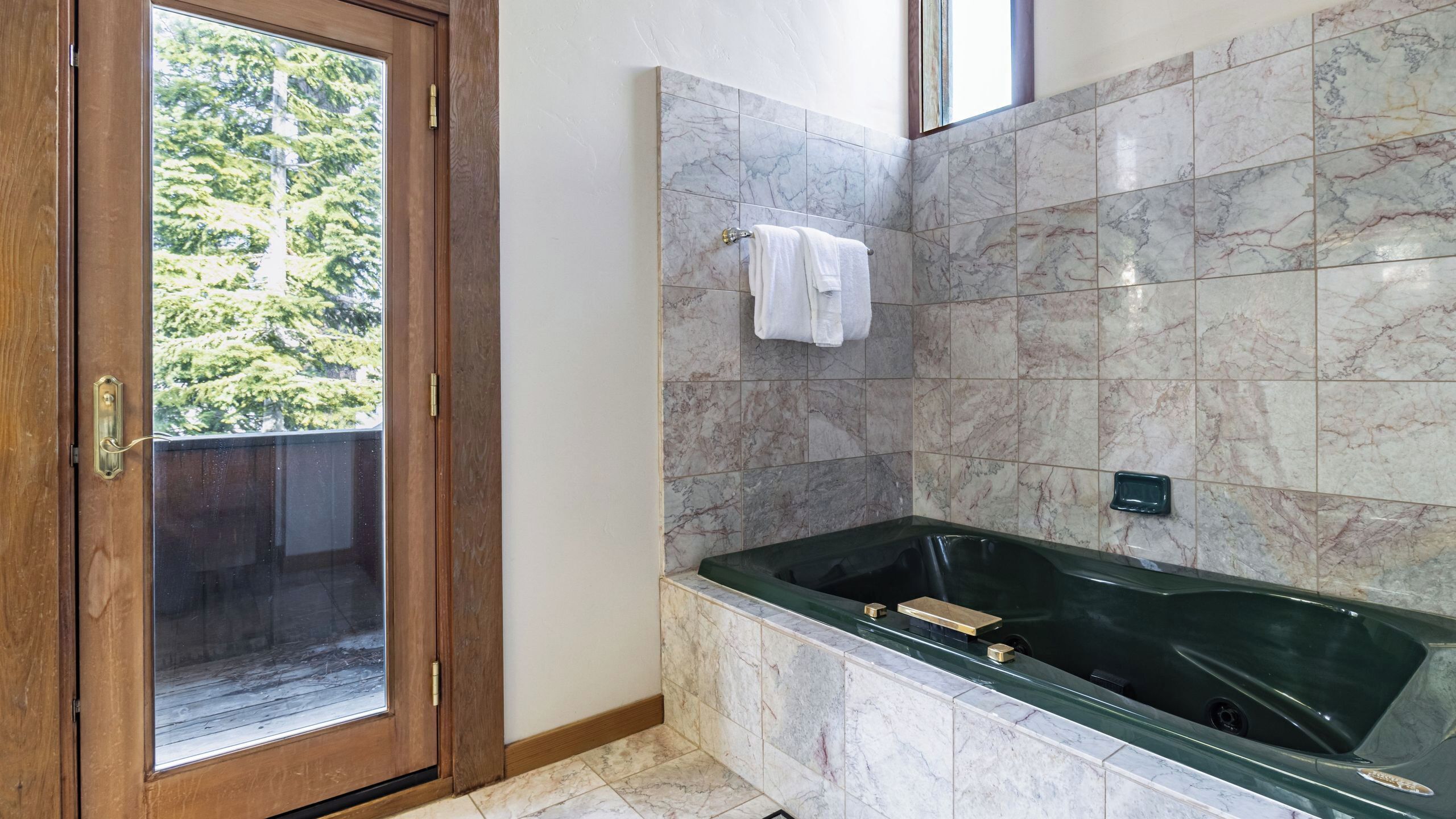 Un baño con ducha de mampara de vidrio, paredes de mármol y una bañera verde.