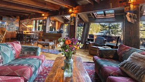 A cozy cabin interior with wooden beams, a dining area, and a large window with a view of trees. - Walk to Palisades Village + Ski Lifts 5BR w/ Mtn Views Mt. Jola by Avantstay (Olympic Valley)