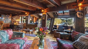 A cozy cabin interior with a dining area, wooden furniture, and a large window offering a view of the outdoors. - Walk to Palisades Village + Ski Lifts 5BR w/ Mtn Views Mt. Jola by Avantstay (Olympic Valley)