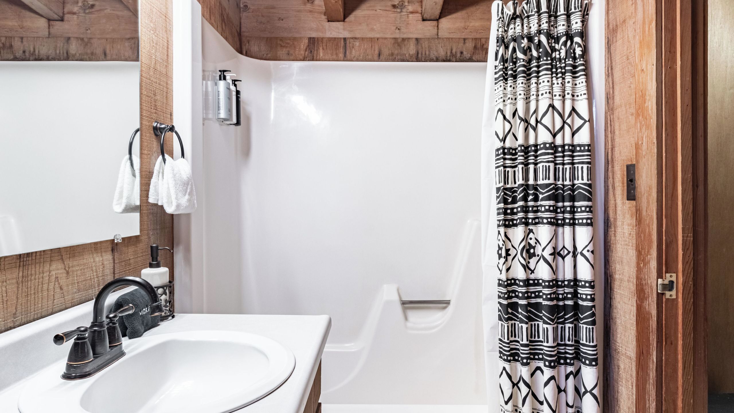 A bathroom with a white sink, black faucet, and a shower curtain with a geometric pattern.