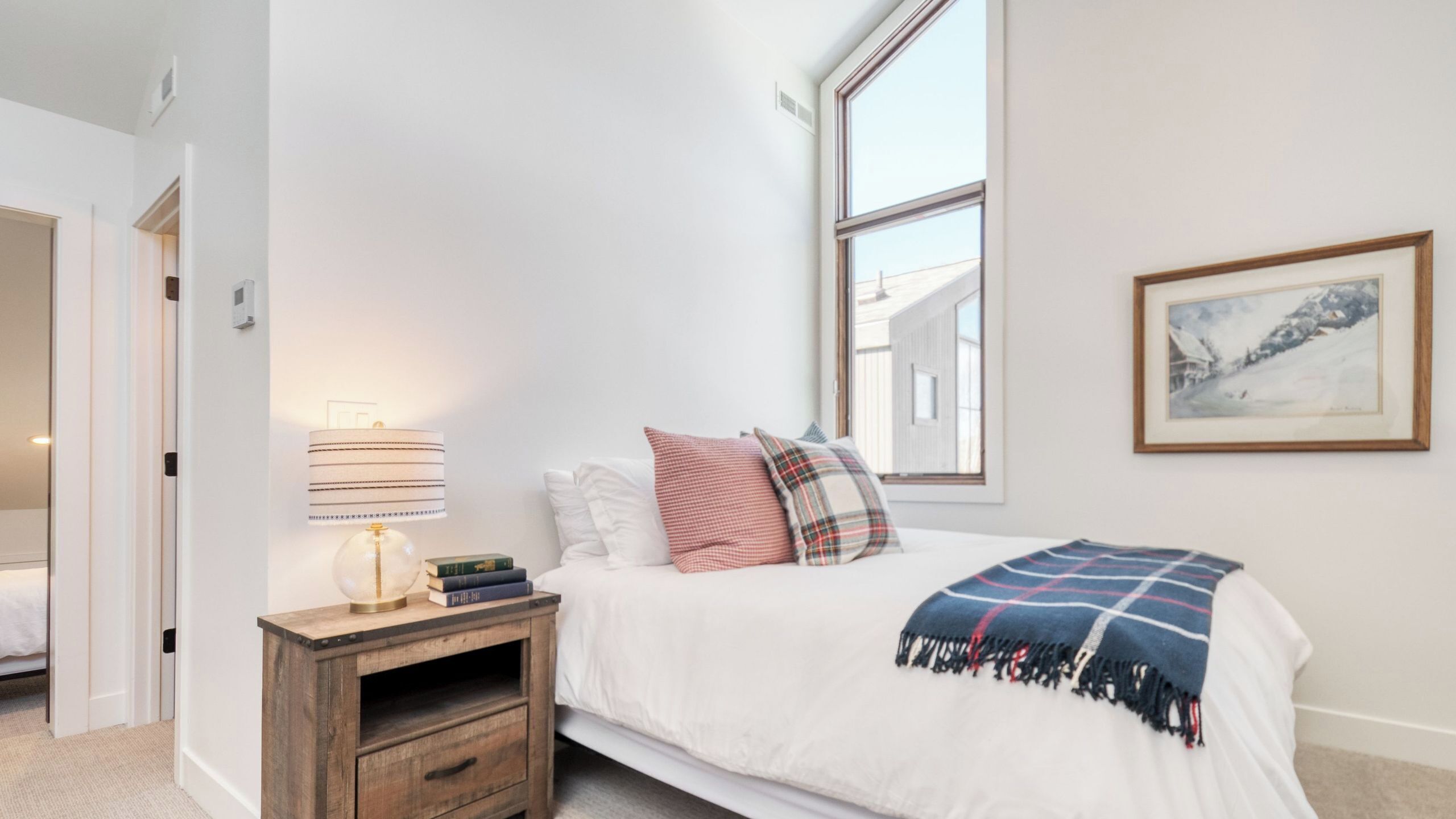 A bedroom with a bed, bedside table, lamp, and a window with a view.