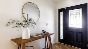 A wooden console table with a white vase and books, a round mirror, and a black door with a window. - Cabernet By Avantstay Tranquil Sonoma Valley Oasis w/ Pool & Fire Pit (Santa Rosa)