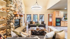 A cozy living room with a stone fireplace, a chandelier, a sofa, and a coffee table. - River Rock by Avantstay Sleeps 20 w/ Hot Tub + Game Room & Theater 10 Min Walk to Mtn (Breckenridge)