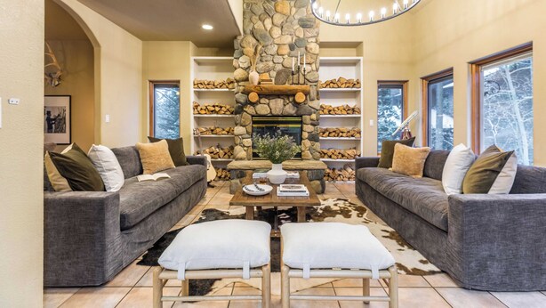 A cozy living room with two grey sofas, a stone fireplace, and a chandelier. - River Rock by Avantstay Sleeps 20 w/ Hot Tub + Game Room & Theater 10 Min Walk to Mtn (Breckenridge)