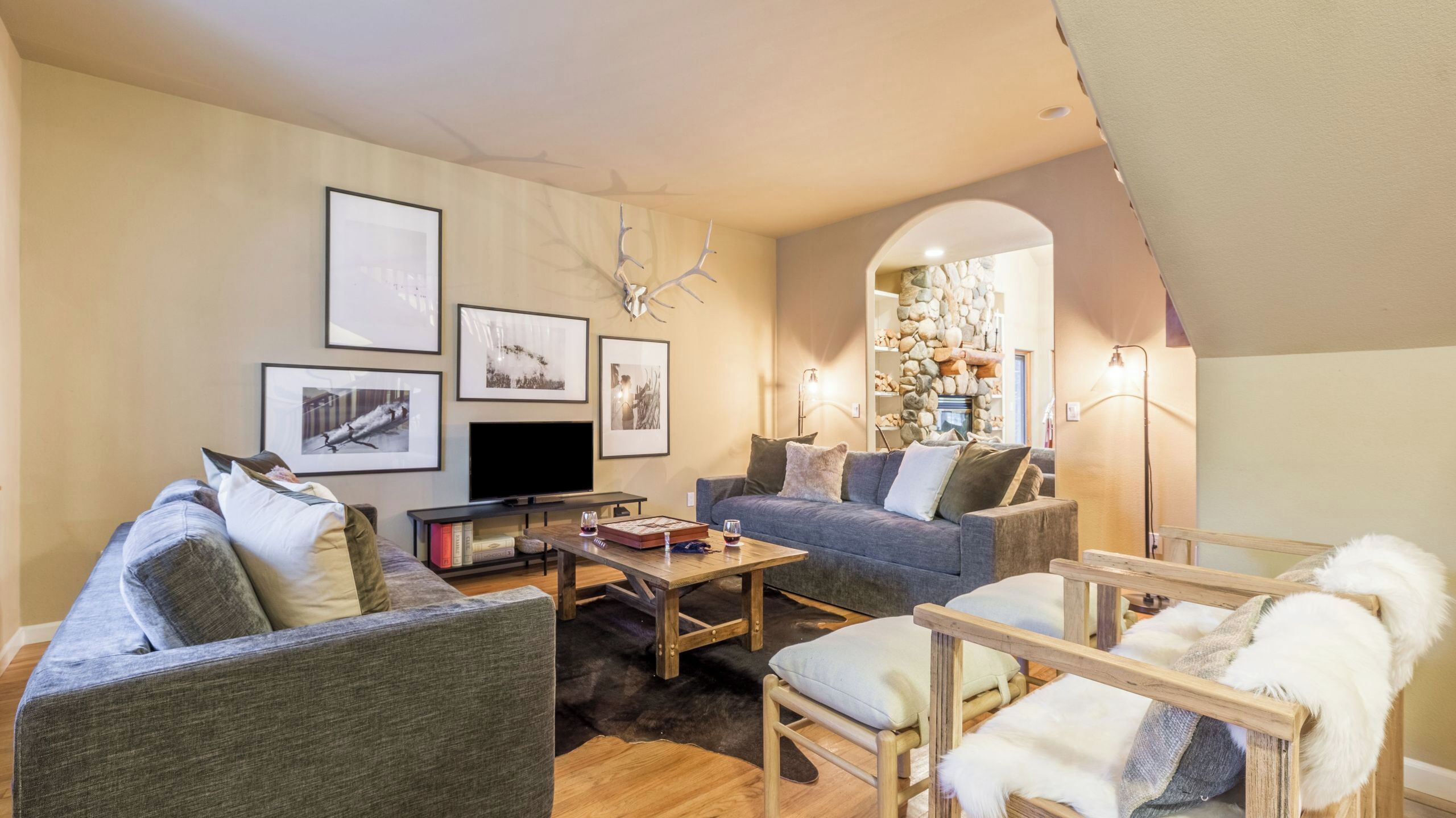 A living room with a sofa, chairs, a coffee table, a TV, framed pictures, and a stone fireplace.