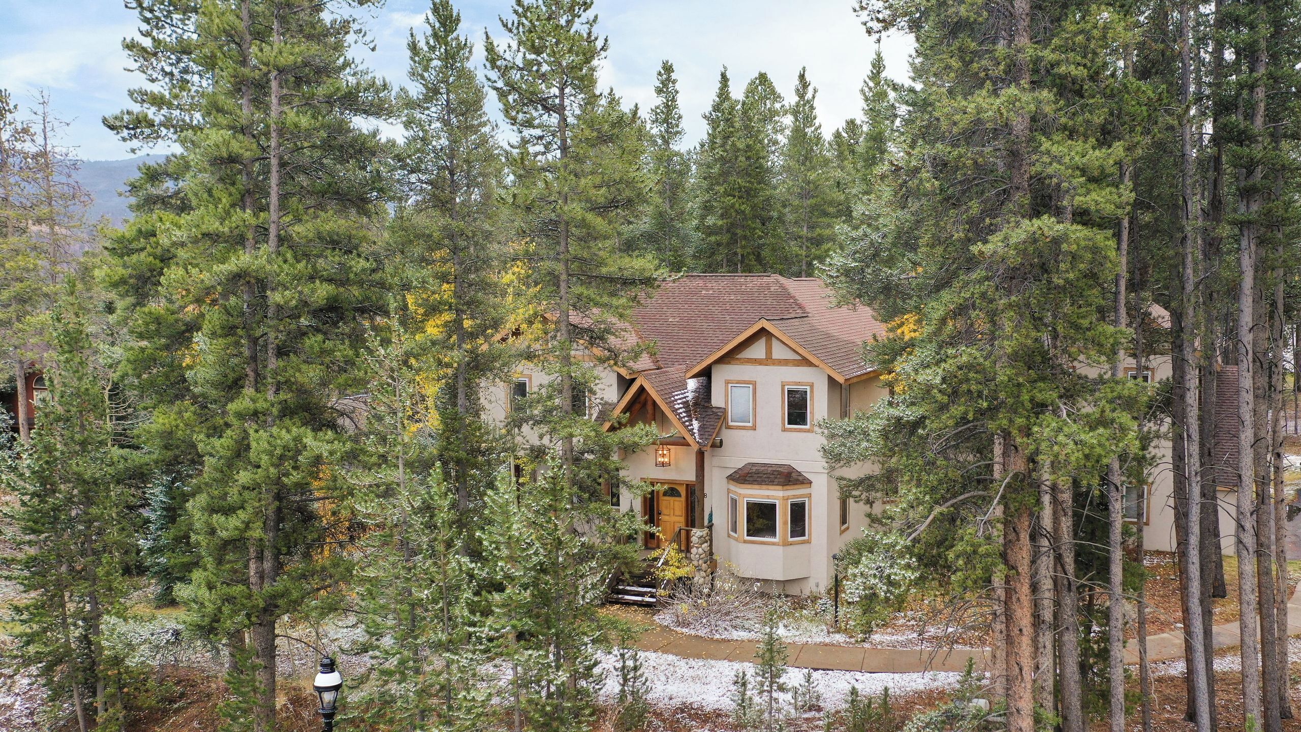A two-story house surrounded by tall pine trees with a stone staircase leading to the entrance.