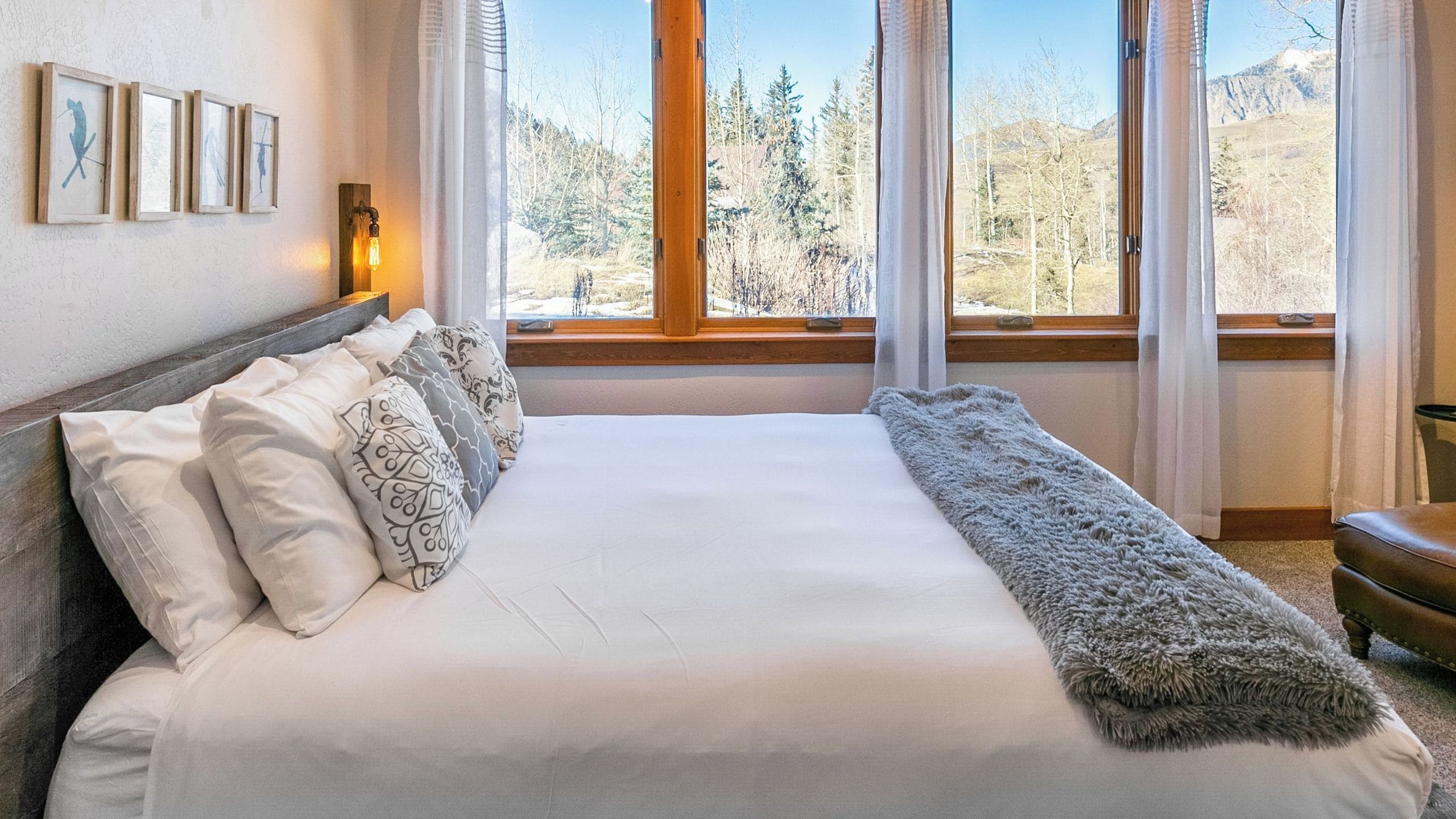 Ein Schlafzimmer mit einem großen Bett, einem Fenster mit Blick auf Bäume und Berge sowie gerahmten Kunstwerken an der Wand.