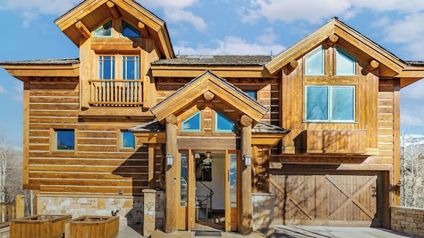 A log cabin with a stone fireplace, a wooden deck, and a garage.