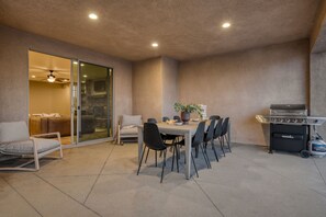 Une terrasse extérieure équipée d’une table à manger, de chaises, d’un barbecue et d’une porte-fenêtre coulissante donnant sur un espace de vie.