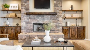 A living room with a stone fireplace, wooden shelves, a flat-screen TV, and a coffee table with decorative items. - Gambel by Avantstayjtree Escape w/ Entertainers Yard, & Firepit, 3000sf (Yucca Valley)