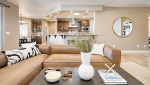 A modern living room with a brown leather sofa, a white vase with flowers, and a coffee table with snacks and drinks. - Gambel by Avantstayjtree Escape w/ Entertainers Yard, & Firepit, 3000sf (Yucca Valley)