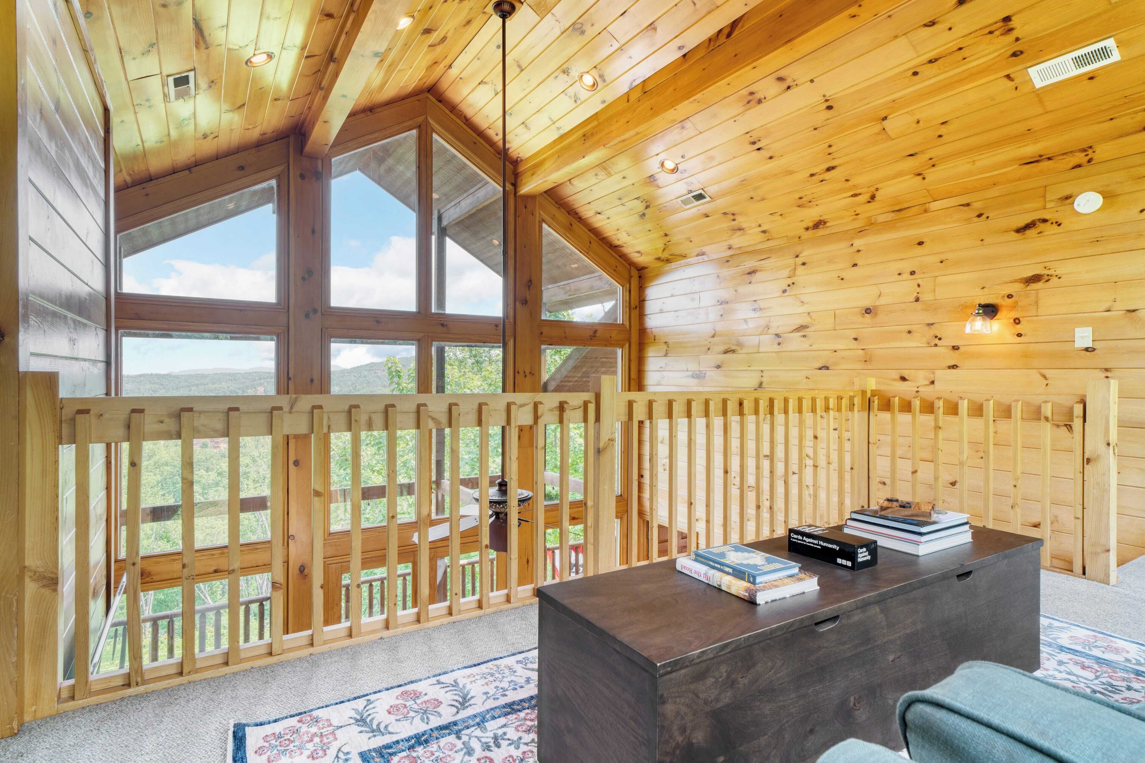Interno di una baita in legno con ampie finestre, un tavolo di legno scuro e vista sull'esterno.