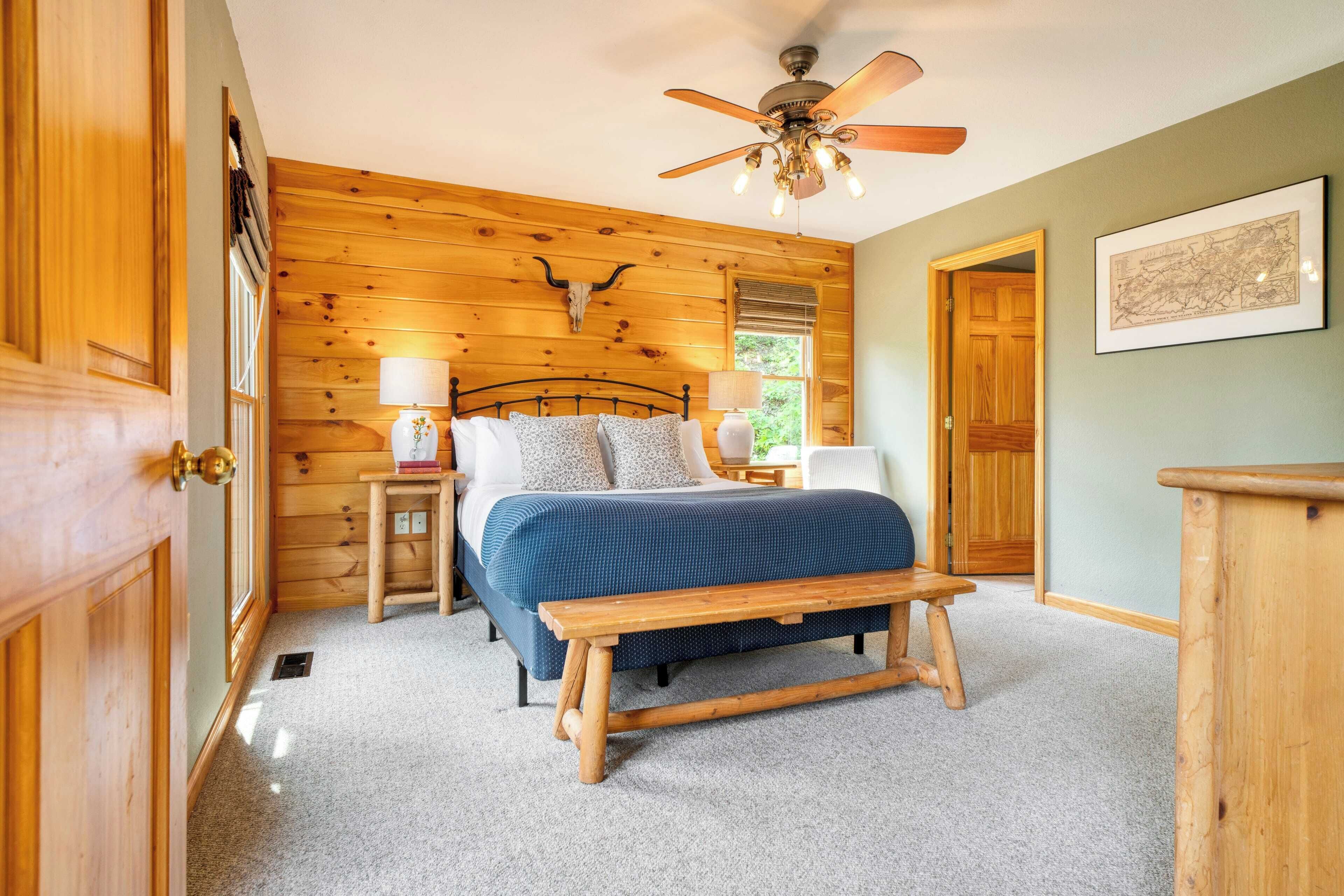 A bedroom with a wooden bed, a bench, a nightstand, a ceiling fan, and a framed map on the wall.