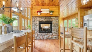 A wooden interior with a stone fireplace, dining table, chairs, and a refrigerator.