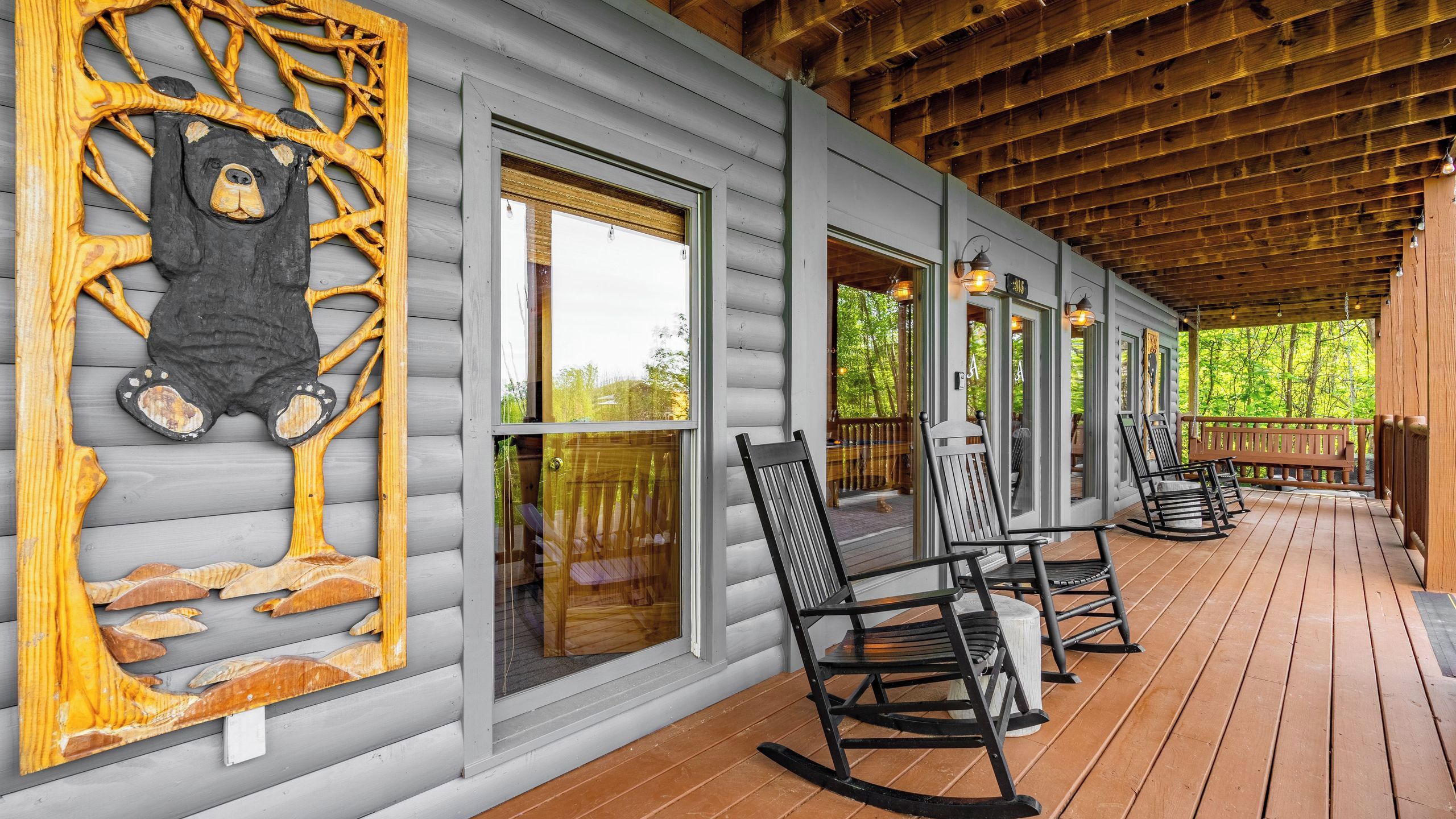 A covered porch with wooden flooring, rocking chairs, and a bear sculpture on the wall.