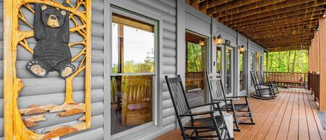 A covered porch with rocking chairs and a large bear sculpture on the wall.