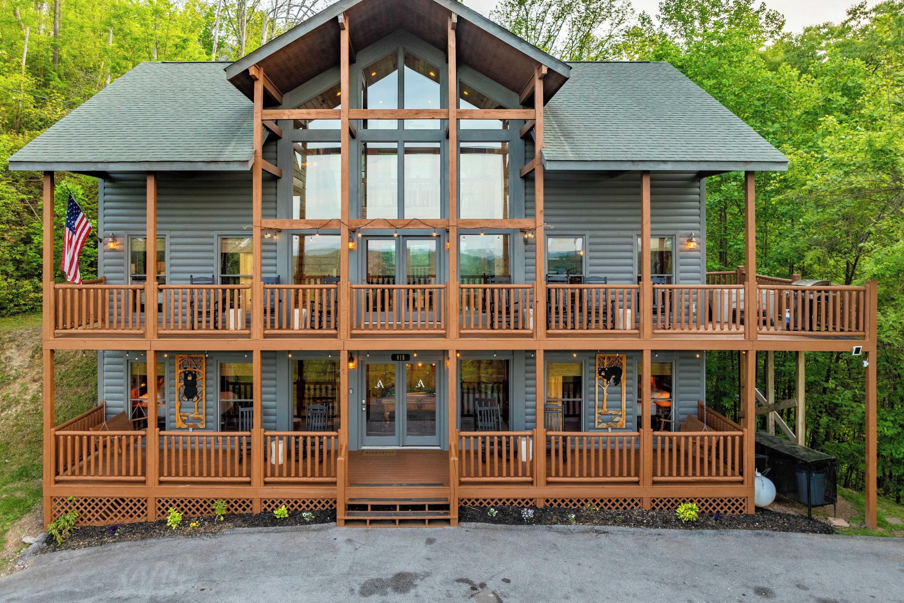 A multi-story log cabin with a balcony on each floor, featuring a large front entrance and an American flag.