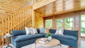 A wooden cabin interior with a blue sofa, a round coffee table, and a staircase.