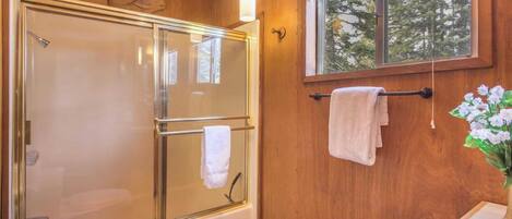 A wooden interior with a glass-enclosed shower, a window with a view of trees, and a towel rack with towels.