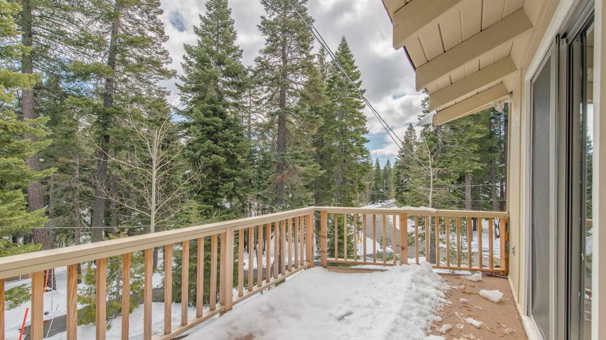 A wooden balcony with a view of a forested area and snow on the ground.