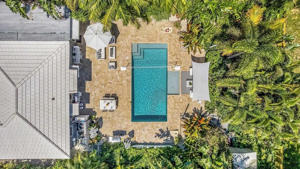Vista aérea de un área de piscina en la azotea con una piscina rectangular, rodeada de sillas de descanso y sombrillas, y exuberante vegetación tropical.