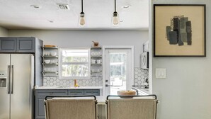Una cocina moderna con refrigerador empotrado, gabinetes blancos, un salpicadero hexagonal y dos sillas en una mesa con un bol de limones.