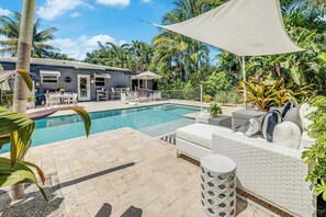 Ein Poolbereich mit einer weißen Outdoor-Lounge, einem kleinen Tisch und einer überdachten Sitzgelegenheit.