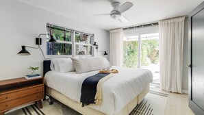 Un dormitorio con cama, mesita de noche, lámpara, ventana y cortinas.