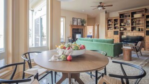 Un coin repas avec une table ronde, des chaises, un saladier de fruits et un ventilateur de plafond.
