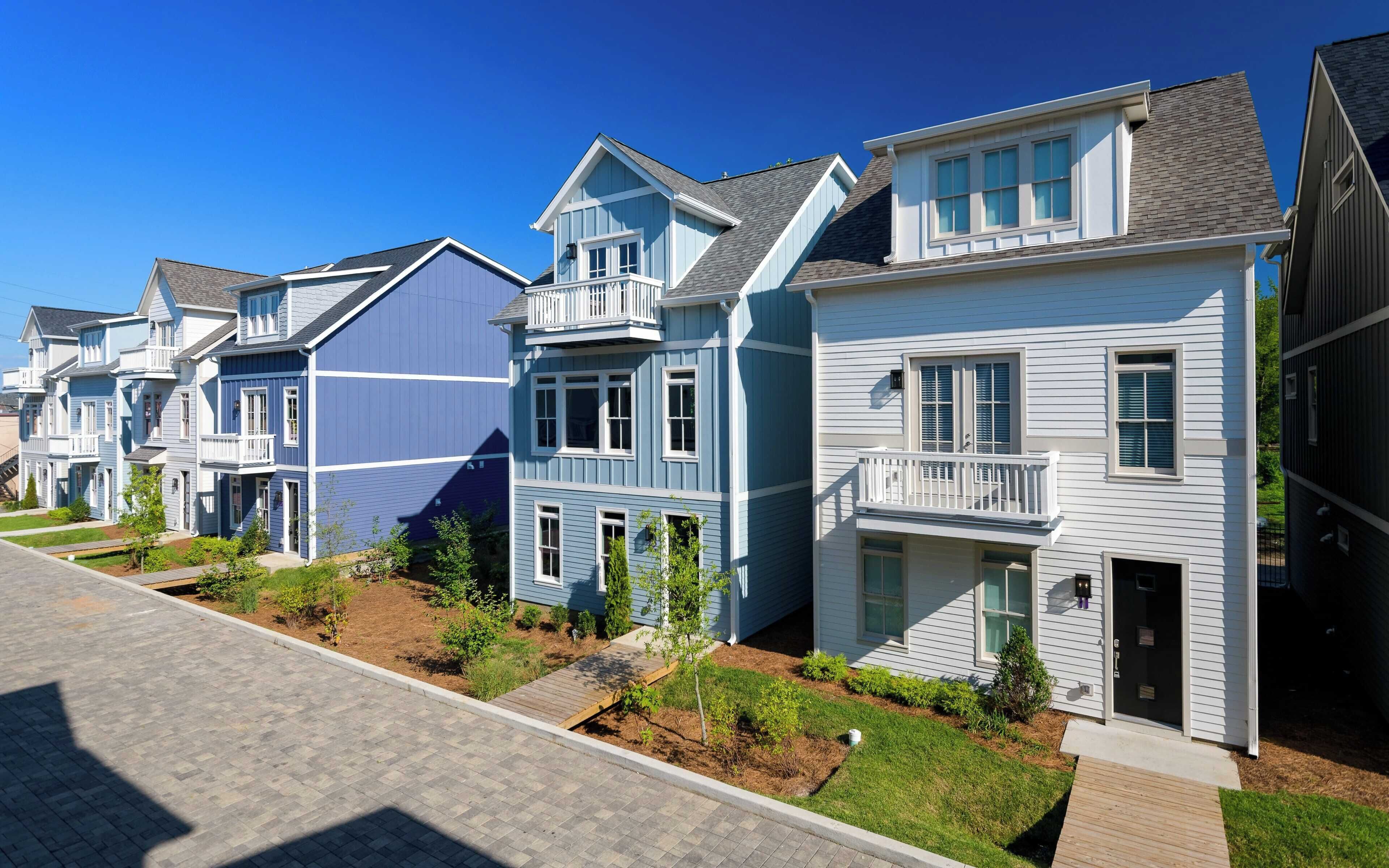 A row of townhouses with front porches, a paved driveway, and a well-maintained lawn.
