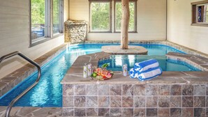 Una piscina interior con baldosas de piedra, una terraza de madera y una pared de piedra.