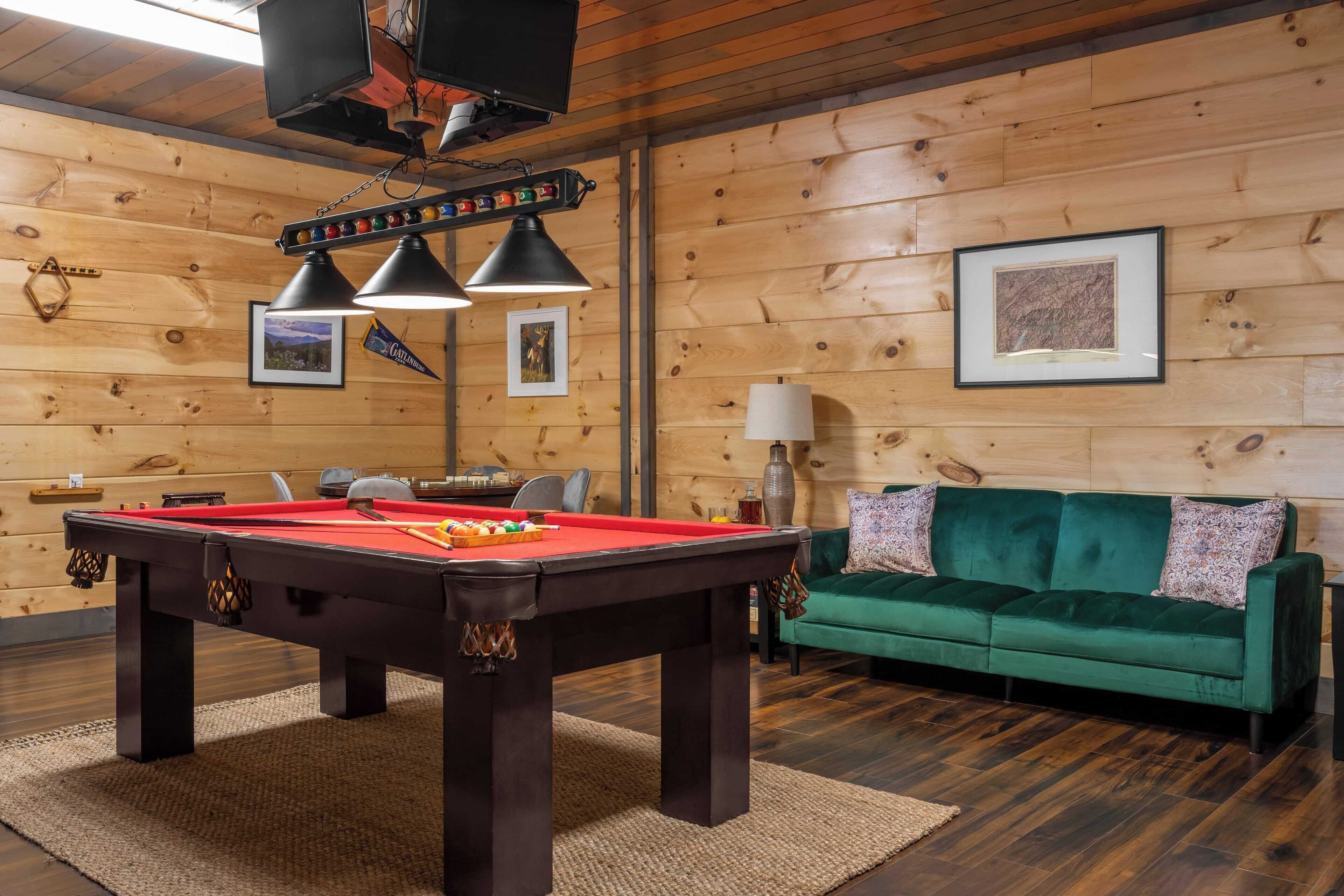 A wooden-paneled room with a pool table, a green sofa, and a framed picture on the wall.