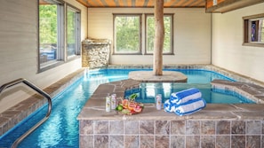 Une piscine intérieure avec un mur en pierre, une terrasse en bois et un jacuzzi en pierre.