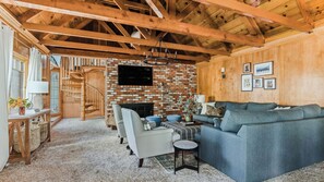 A spacious living room with a brick fireplace, a grey sofa, and a wooden staircase.
