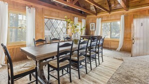A wooden dining room with a large table and chairs, windows with curtains, and a wooden ceiling. - Walk to the Lake, Sand Volleyball Court, Pool Table, Deck Gambler by Avantstay (Big Bear Lake)