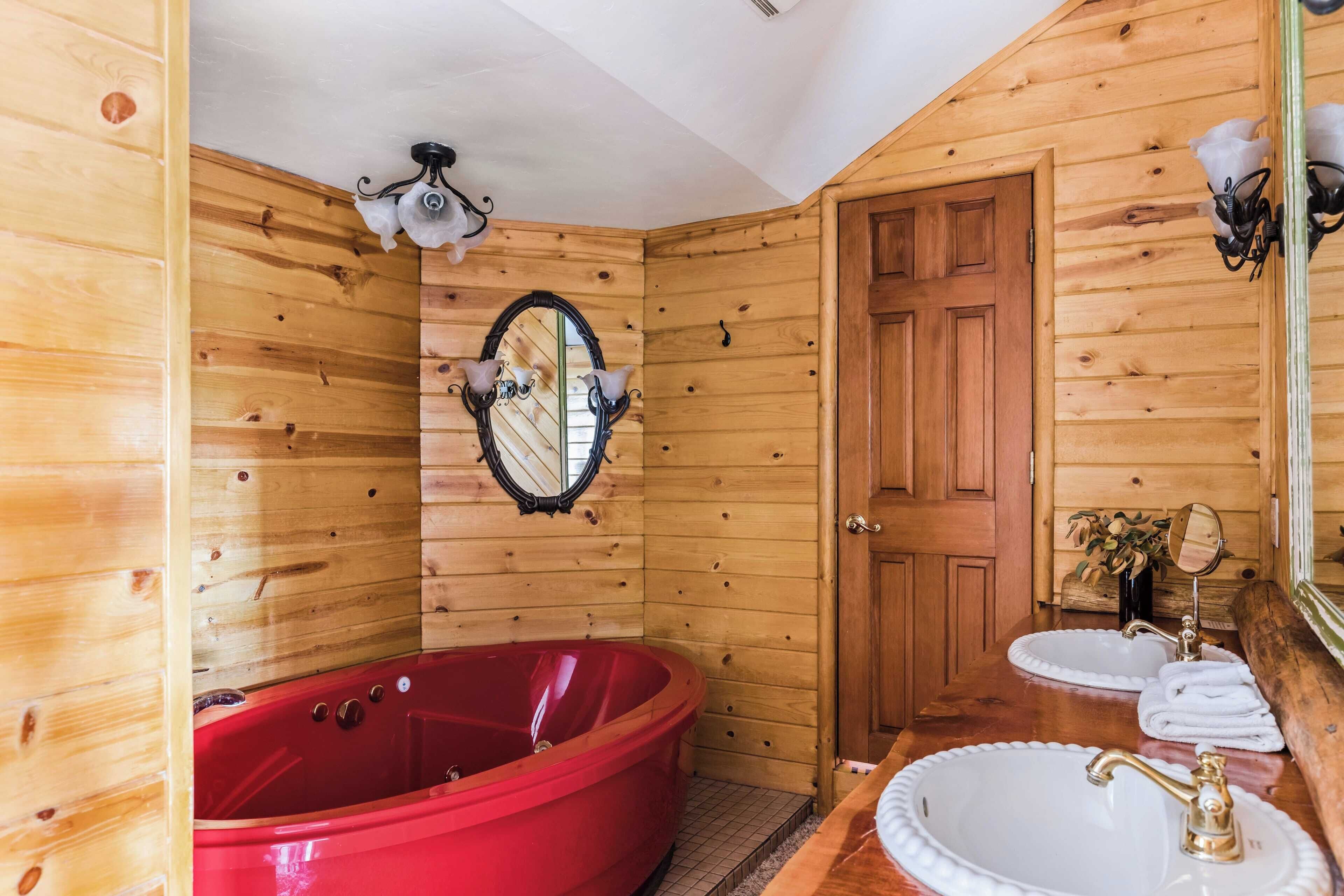 A wooden cabin bathroom with a red bathtub, two sinks, and a mirror.
