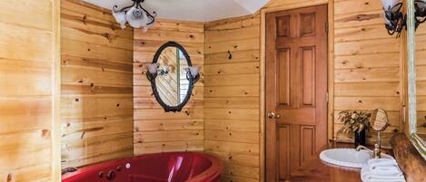 A wooden cabin bathroom with a red bathtub, two sinks, and a mirror.
