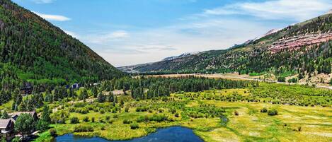 A mountainous landscape with a river, forested areas, and a small settlement with buildings.