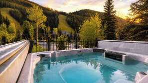 Un bain à remous avec vue sur une montagne boisée et un petit bâtiment en arrière-plan.