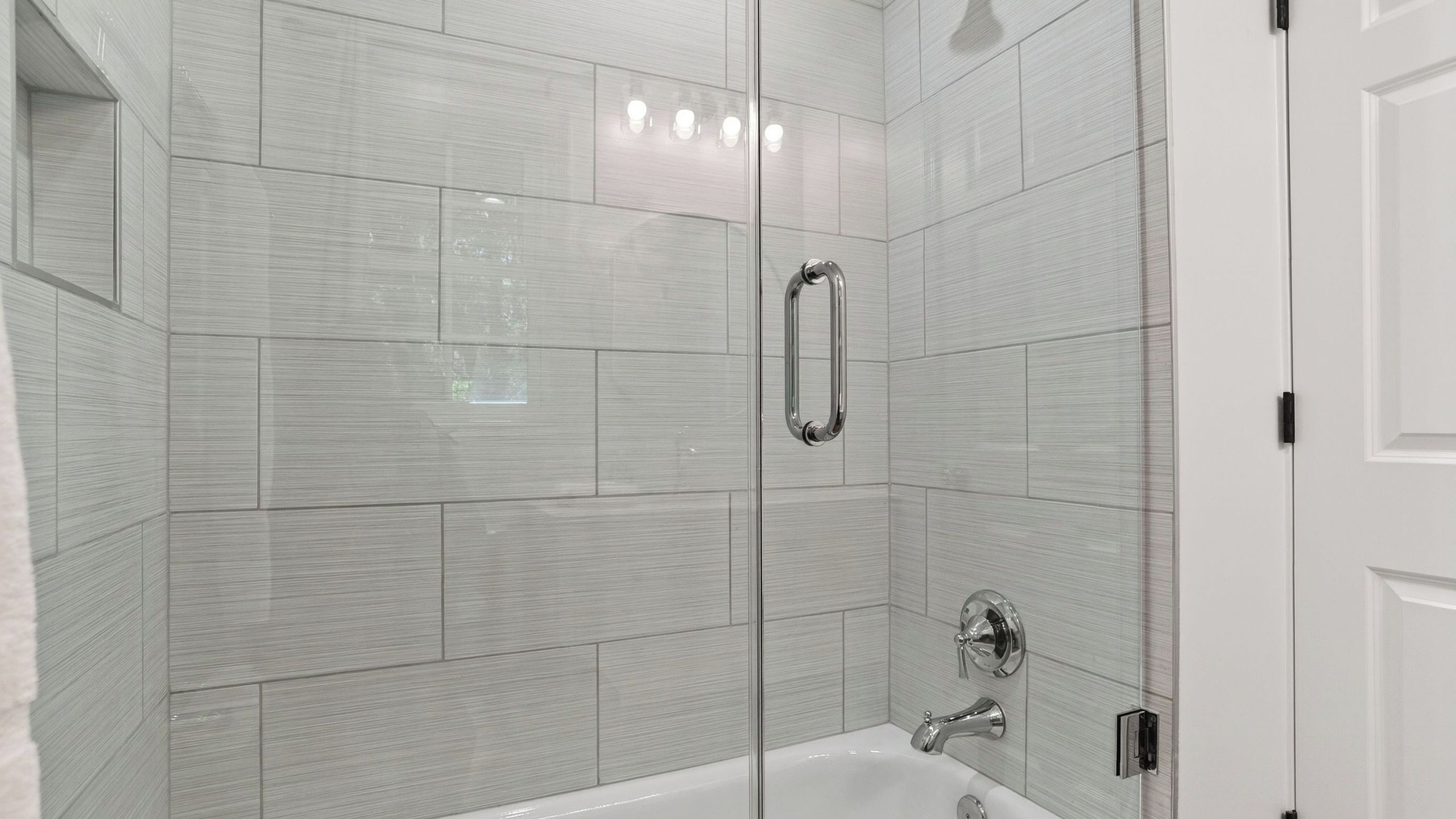 A modern bathroom with a glass shower enclosure, a white bathtub, and a chrome faucet.