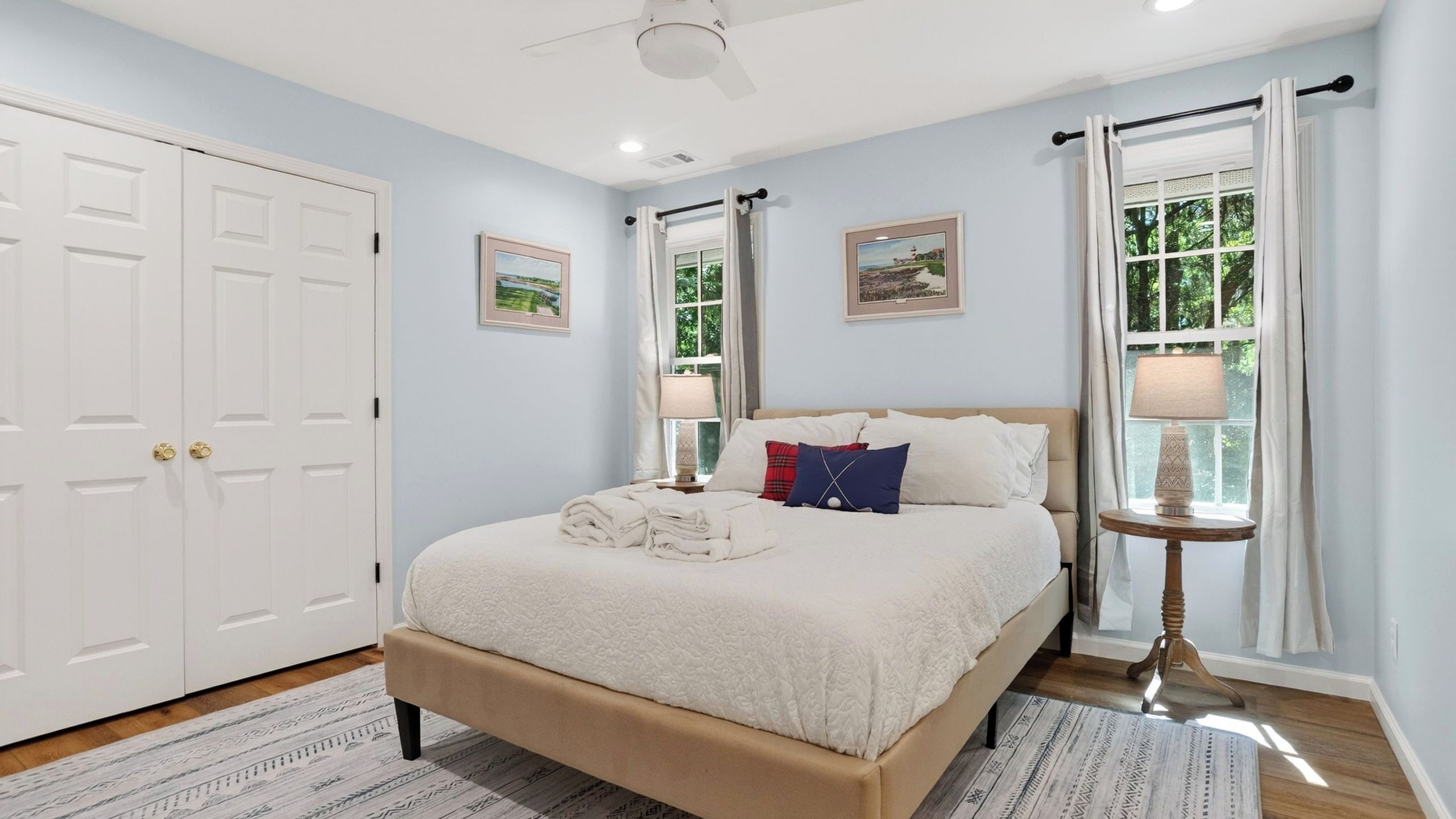 A bedroom with a bed, two bedside tables, a ceiling fan, and a window with curtains.