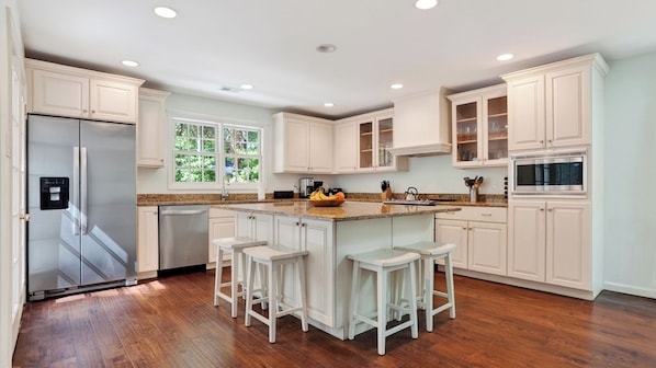 A kitchen with white cabinets, a stainless steel refrigerator, a microwave, and a large island with stools.