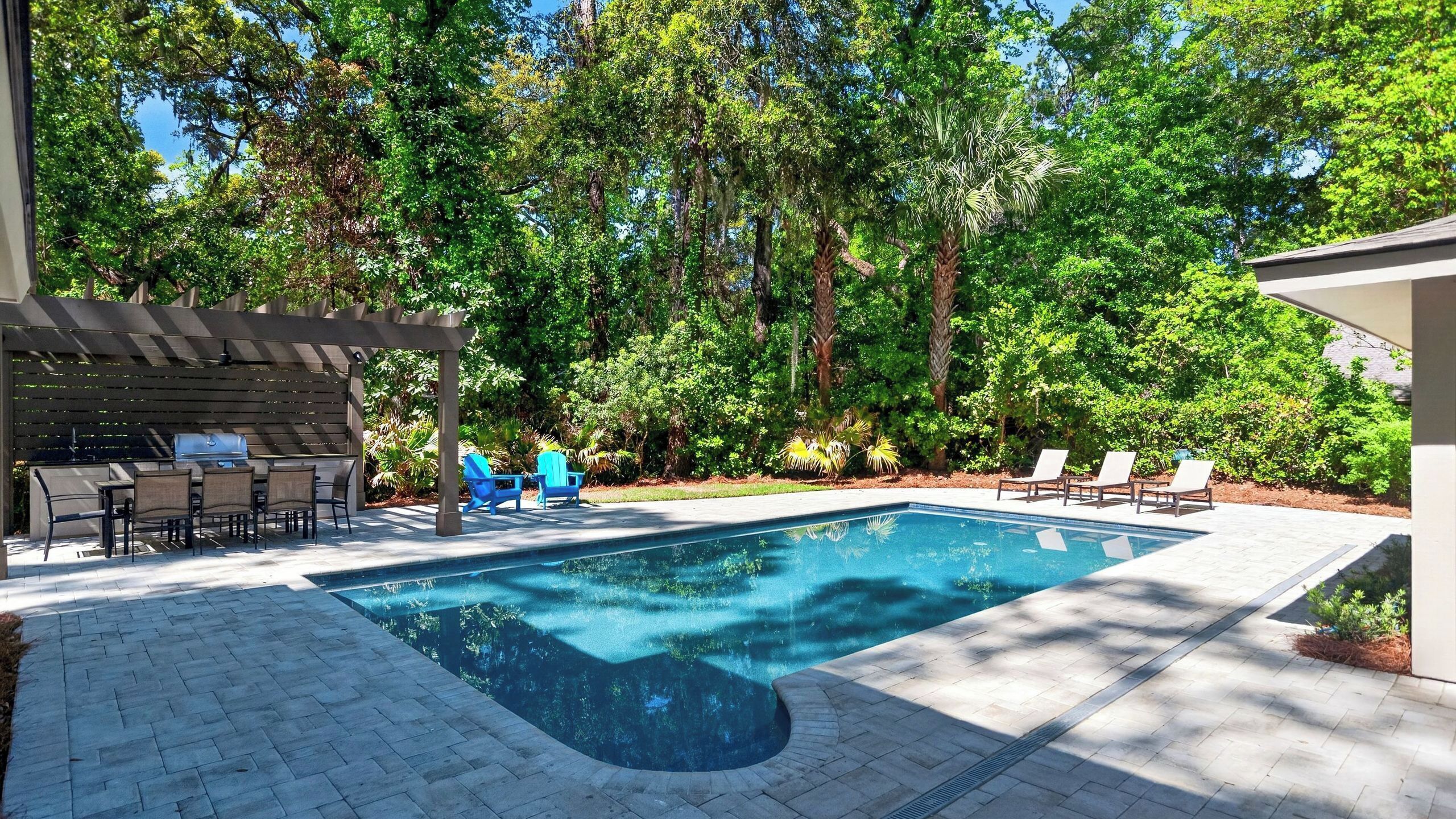 A swimming pool with a pergola and lounge chairs, surrounded by trees.