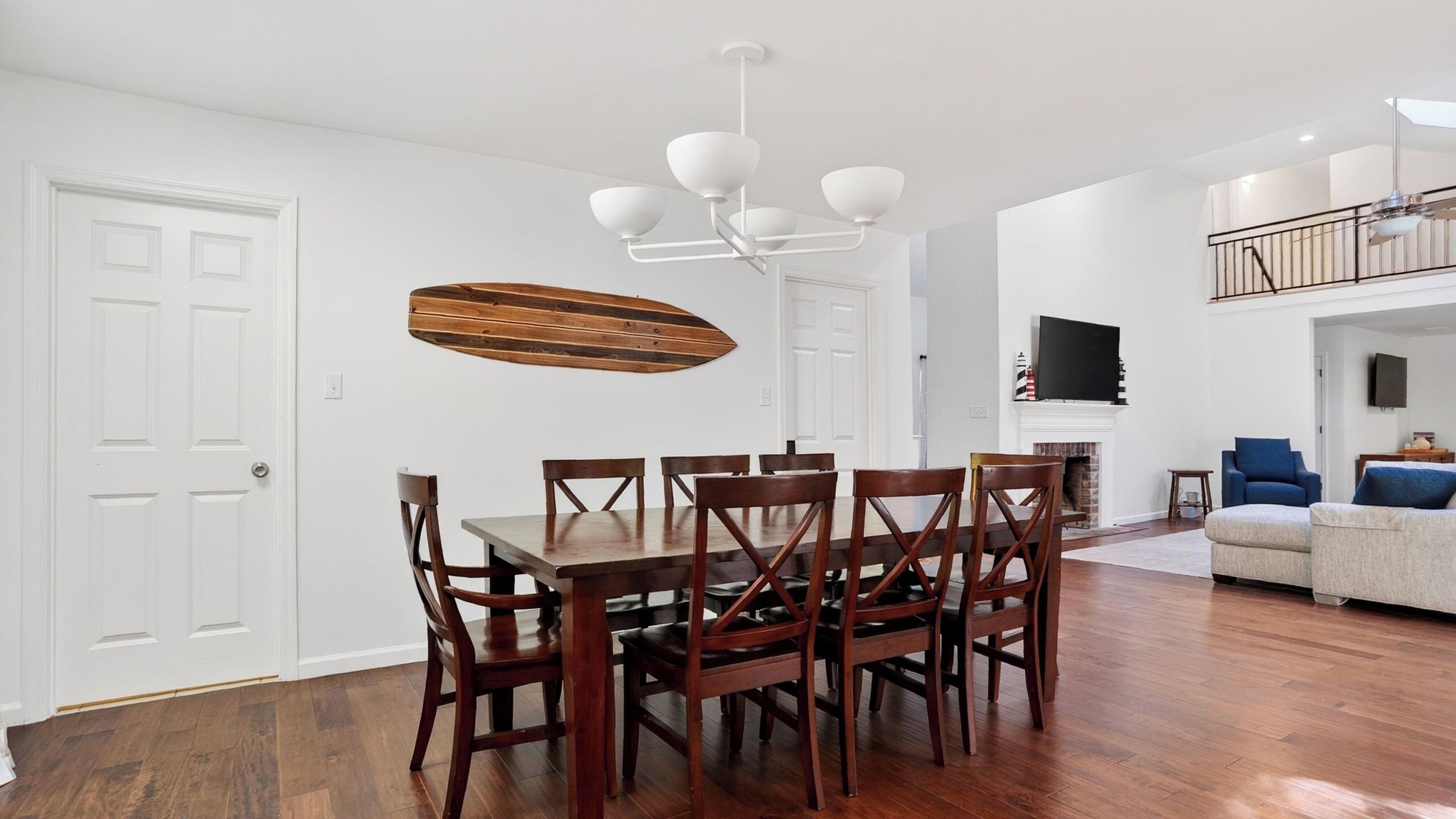 A dining area with a wooden table and chairs, a chandelier, and a fireplace in the background.