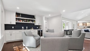 Un salon moderne avec une table de billard, des fauteuils à revêtement gris et un coin bar avec des bouteilles d’alcool.